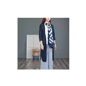 Puede incluir: Un c&aacute;rdigan largo azul marino con mangas tres cuartos, usado sobre una camiseta blanca y pantalones azul claro. Una bufanda a rayas en azul marino y blanco est&aacute; drapeada alrededor del cuello. El atuendo es casual y elegante.