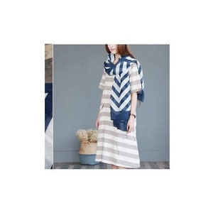 Puede incluir: Una persona con un vestido a rayas y una bufanda con estampado de chevr&oacute;n azul y blanco. El vestido tiene rayas horizontales en tonos neutros. La bufanda est&aacute; drapeada alrededor del cuello y los hombros.