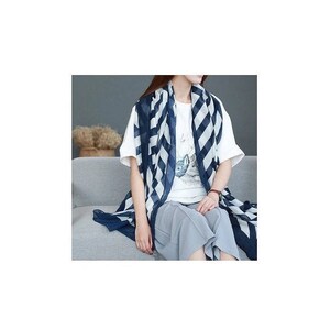 Puede incluir: Una bufanda a rayas azul marino y blanca sobre una camiseta blanca y pantalones grises. La bufanda tiene un patr&oacute;n geom&eacute;trico audaz. La persona est&aacute; sentada en un sof&aacute; gris.