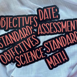 Puede incluir: Una colecci&oacute;n de pegatinas negras con texto color coral que incluye las palabras OBJECTIVES, DATE, ASSESSMENTS, STANDARD, SCIENCE y MATH. Cada pegatina tiene una forma troquelada que sigue el contorno de las letras negritas sin remates.