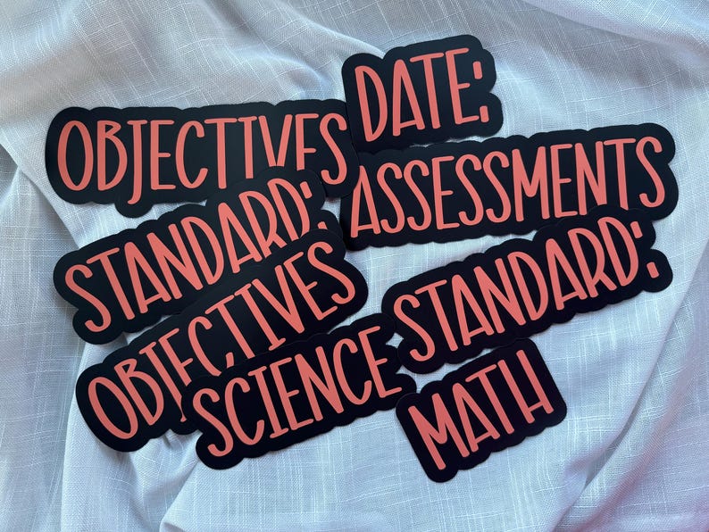 Puede incluir: Una colecci&oacute;n de pegatinas negras con texto color coral que incluye las palabras OBJECTIVES, DATE, ASSESSMENTS, STANDARD, SCIENCE y MATH. Cada pegatina tiene una forma troquelada que sigue el contorno de las letras negritas sin remates.