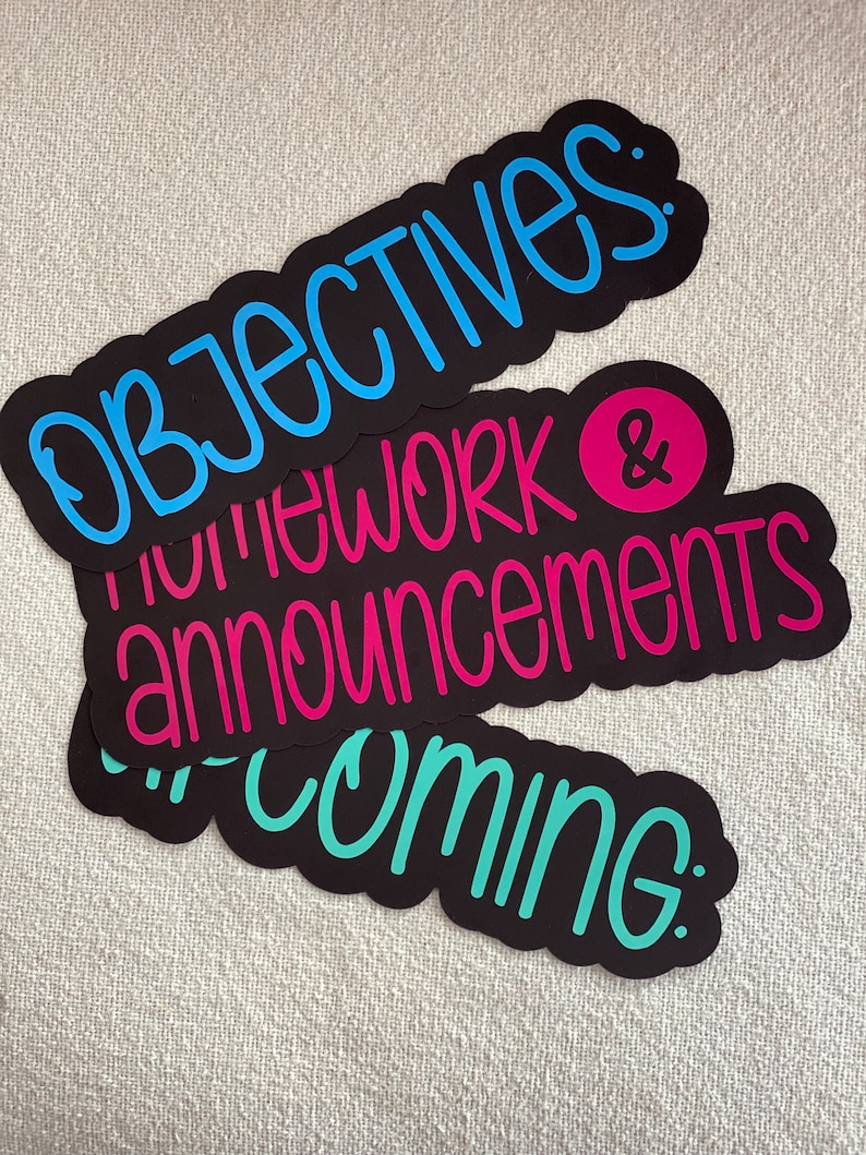 Pu&ograve; includere: Tre adesivi neri fustellati con bordi smerlati. L'adesivo superiore presenta la parola OBJECTIVES: in blu. L'adesivo centrale mostra HOMEWORK & ANNOUNCEMENTS in rosa con una e commerciale in un cerchio rosa. L'adesivo inferiore riporta la scritta UPCOMING: in verde acqua.