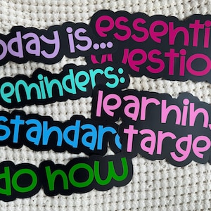 Pu&ograve; includere: Un set di adesivi neri fustellati con testo colorato. Gli adesivi presentano le frasi today is, essential question, reminders, learning target, standard e do now in caratteri viola, rosa, turchese, blu e verdi con contorni neri.