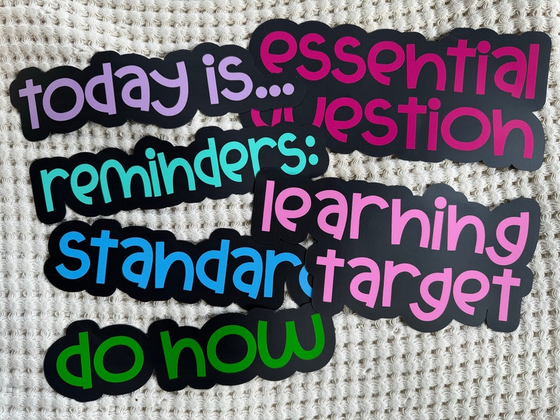 Pu&ograve; includere: Un set di adesivi neri fustellati con testo colorato. Gli adesivi presentano le frasi today is, essential question, reminders, learning target, standard e do now in caratteri viola, rosa, turchese, blu e verdi con contorni neri.