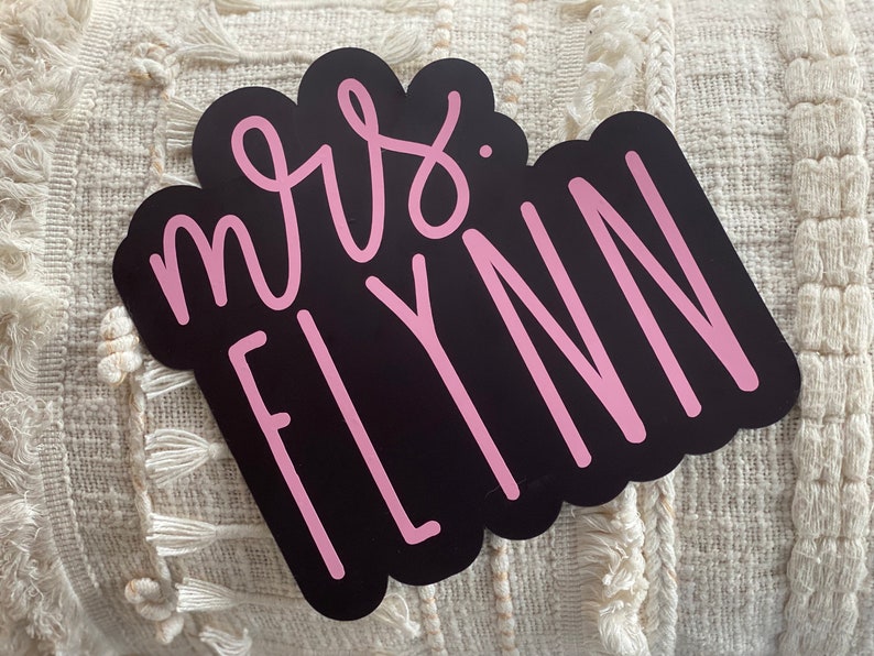 Puede incluir: Pegatina de vinilo negro y rosa con el texto "mrs. FLYNN" en una fuente cursiva.