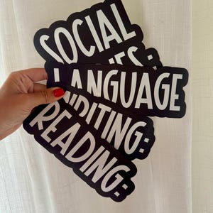 May include: A stack of three black die-cut stickers with white text. The top sticker reads SOCIAL, the middle sticker reads LANGUAGE, and the bottom sticker reads READING: EDITING:. Each sticker features a bold, sans-serif font with a thick black border.