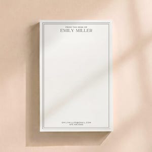 May include: A rectangular white notepad featuring a thin black double-line border. The top center text reads FROM THE DESK OF EMILY MILLER. The bottom center text displays EMILYMILLER@EMAIL.COM and 619.456.5555 in a clean black font.