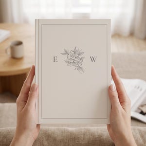 Peut inclure: Un livre à couverture rigide de couleur crème avec une fine bordure rectangulaire, la lettre E à gauche, la lettre W à droite et une illustration centrale au trait représentant un bouquet floral dans une encre gris foncé.