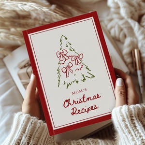 May include: A rectangular recipe book with a white cover, a thick red border, and a green line-art Christmas tree illustration featuring three red bows. The text reads "MOM'S Christmas Recipes" in red lettering centred below the tree graphic.