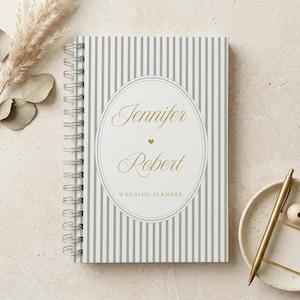 May include: A spiral-bound wedding planner notebook featuring a gray and white vertical striped cover. A central white oval contains the gold text Jennifer and Robert with a small heart icon and the words WEDDING PLANNER printed below.
