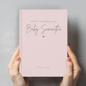 Puede incluir: Un diario de bebé rosa claro con el texto "Sweet Wishes For Baby Samantha" en escritura elegante. La fecha "July 5, 2026" está impresa en la parte inferior. Un pequeño corazón está entre el nombre y el texto.