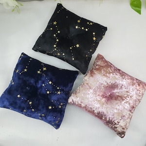 May include: Three velvet pillow cushions with gold star patterns. One is black, one is blue, and one is pink.