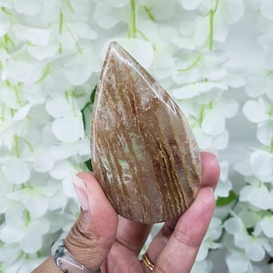 May include: A teardrop-shaped polished stone with brown and white stripes. The stone is translucent and has a smooth, polished surface.