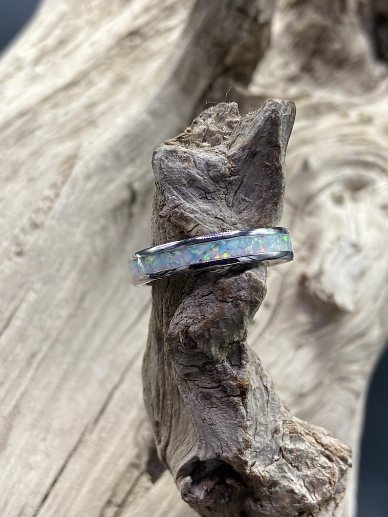 May include: A silver ring with a white opal inlay. The ring is displayed on a piece of driftwood.