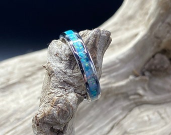 May include: A silver ring with a blue opal inlay. The ring is on a piece of driftwood.