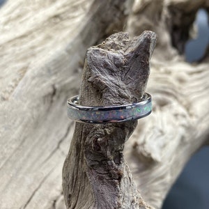 May include: A silver ring with a thin band and a white opal inlay. The opal has a rainbow of colors, including pink, green, and blue.