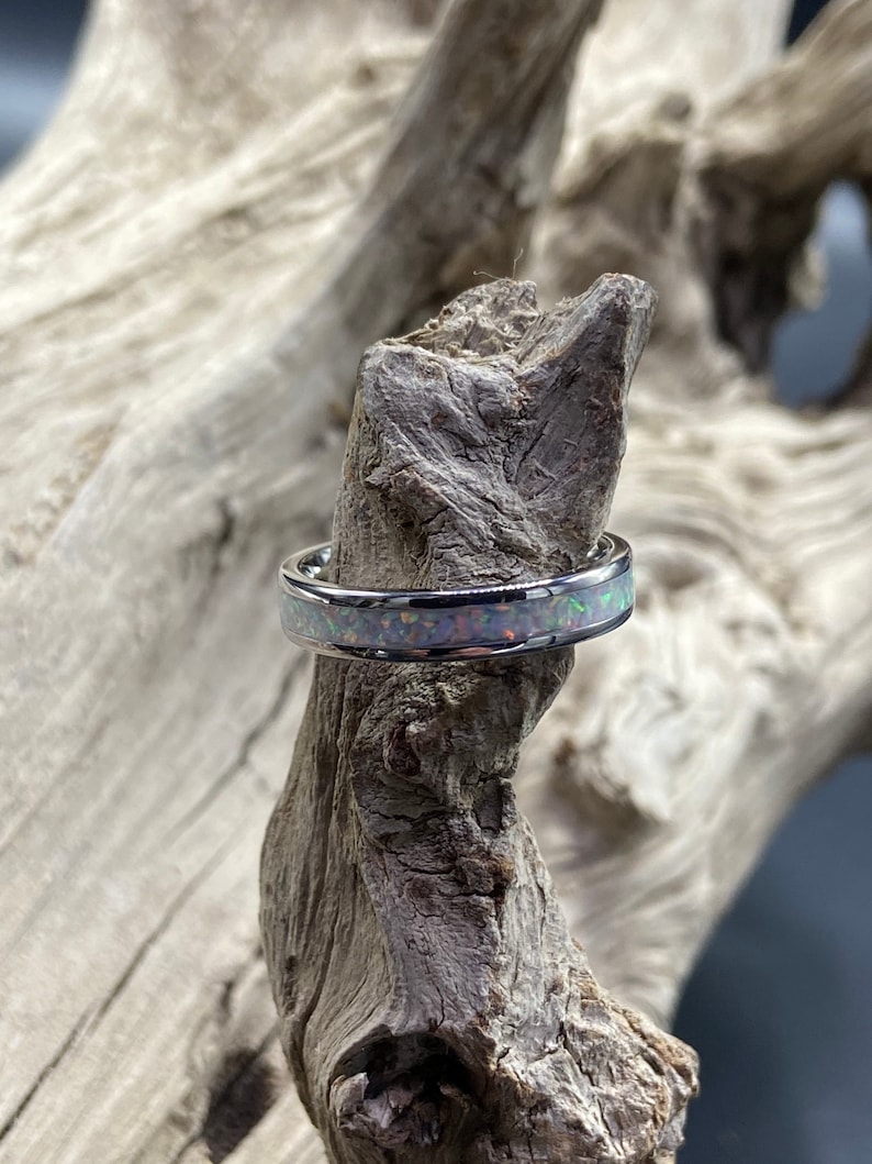 May include: A silver ring with a thin band and a white opal inlay. The opal has a rainbow of colors, including pink, green, and blue.