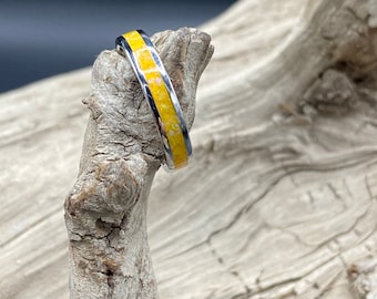 May include: A silver ring with a yellow band of opal inlay. The ring is sitting on a piece of driftwood.