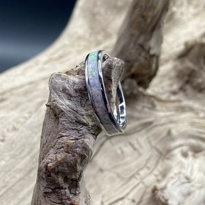 May include: A silver ring with a white opal inlay. The ring is shown on a piece of driftwood.