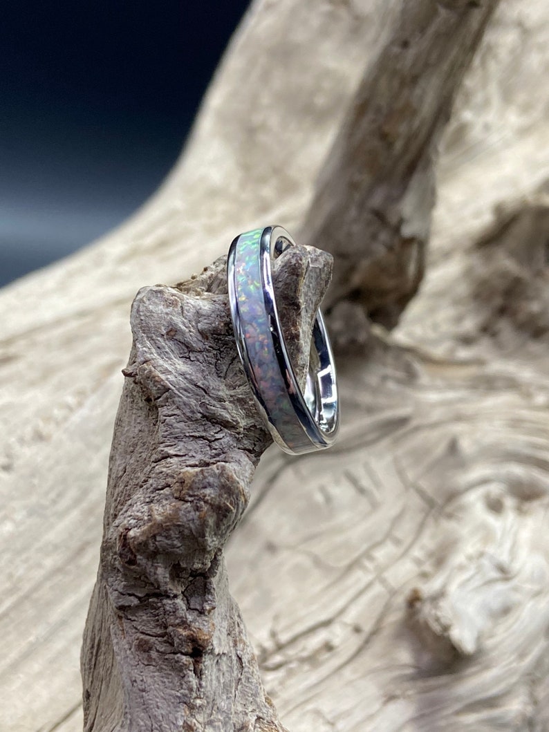 May include: A silver ring with a white opal inlay. The ring is shown on a piece of driftwood.