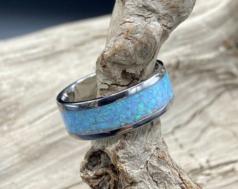 May include: A silver ring with a blue opal inlay. The ring is sitting on a piece of driftwood.