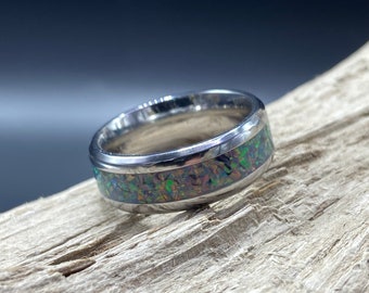 May include: A silver ring with a green and purple opal inlay. The ring is on a piece of driftwood.