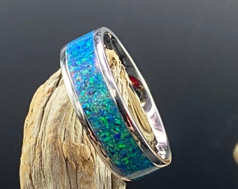 May include: A silver ring with a blue and green opal inlay. The ring is set on a piece of driftwood.