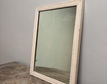 May include: A white framed mirror with a simple design. The mirror is rectangular and has a slightly distressed finish.