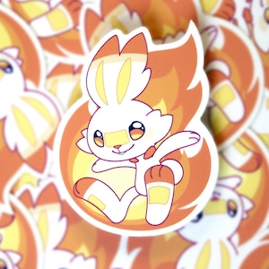 May include: A close-up of a white rabbit with orange ears and a yellow tail, surrounded by flames. The rabbit is wearing a bandage on its right foot and has a bandage on its left ear. The rabbit is smiling and has its eyes closed.