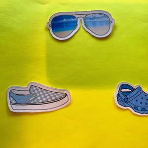 Puede incluir: Una colecci&oacute;n de pegatinas con tem&aacute;tica de verano sobre un fondo amarillo. Las pegatinas incluyen un par de gafas de sol de aviador con una escena de playa reflejada en las lentes, un zapato sin cordones a cuadros azules y blancos y un zueco azul.