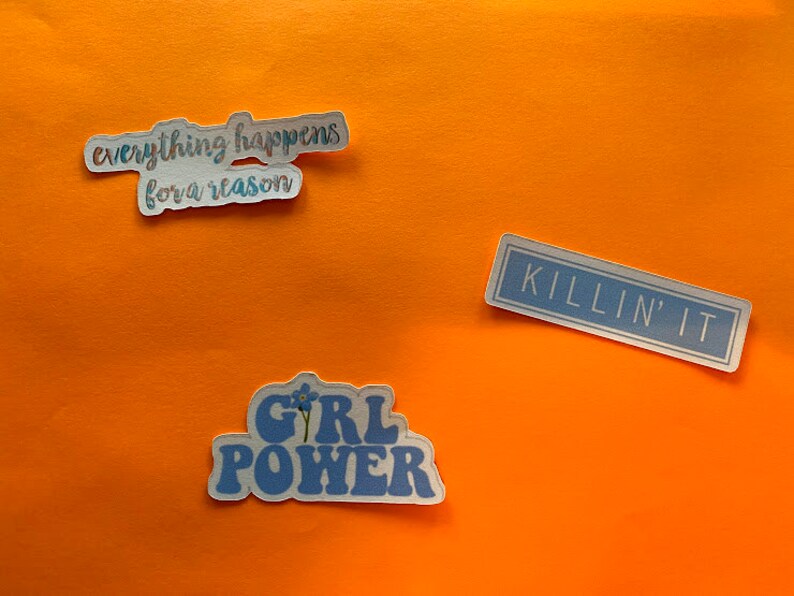 Puede incluir: Tres pegatinas con texto sobre un fondo naranja. Una pegatina dice "everything happens for a reason", otra dice "KILLIN' IT", y la tercera dice "GIRL POWER" con un dise&ntilde;o floral. Las pegatinas tienen una combinaci&oacute;n de colores azul y blanco.