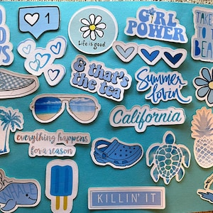 Puede incluir: Una colecci&oacute;n de pegatinas azules y blancas sobre un fondo turquesa. Las pegatinas presentan varios dise&ntilde;os, incluyendo textos como "No Bad Days", "Girl Power" y "Take Me To The Beach". Otros dise&ntilde;os incluyen una margarita, gafas de sol, un zapato y una ballena.