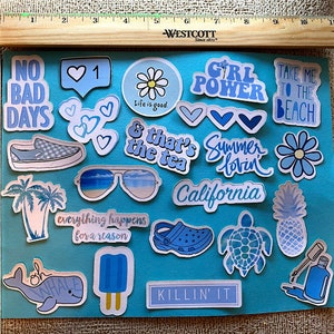 Puede incluir: Un conjunto de pegatinas azules con varios dise&ntilde;os y textos, incluyendo frases como "No Bad Days", "Girl Power" y "Take Me to the Beach". Las pegatinas presentan im&aacute;genes de corazones, flores, gafas de sol y una pi&ntilde;a. Las pegatinas est&aacute;n sobre un fondo azul.