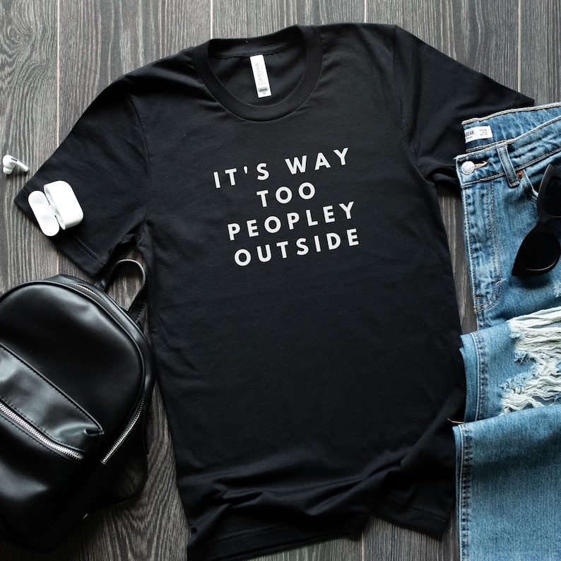 May include: Black t-shirt with white text that reads "It's Way Too Peopley Outside".