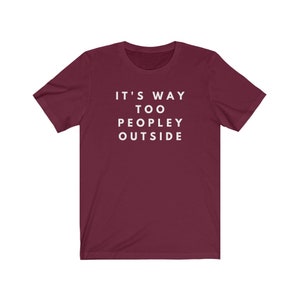 May include: Burgundy short-sleeved t-shirt with white text that reads "It's Way Too Peopley Outside".