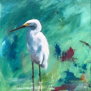 May include: A white egret with a yellow beak stands in a green and blue abstract background. The bird is in focus, while the background is blurred.