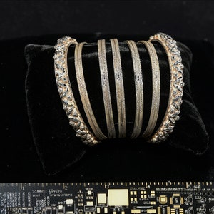 May include: A set of seven silver bangles with intricate designs. The bangles are stacked on top of each other and are displayed on a black velvet surface.
