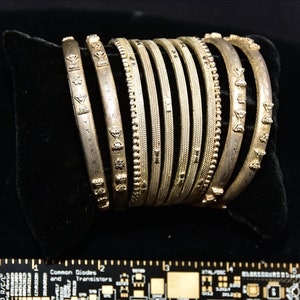 May include: A set of nine silver bangles with intricate designs. The bangles are stacked on top of each other and have a shiny finish.