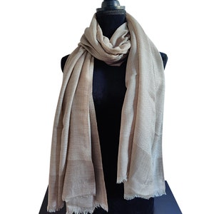 Peut inclure: Écharpe beige drapée sur un mannequin noir. L'écharpe a un aspect doux et fluide avec un bord effiloché. Le tissu semble léger et adapté au superposition. L'écharpe est de couleur neutre, ce qui la rend polyvalente.