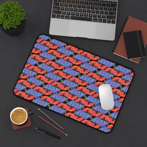 May include: A rectangular mousepad with a repeating pattern of red and blue fan-like shapes on a black background. A white computer mouse sits on the pad, with a laptop and other office supplies in the background.