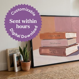 May include: A framed wall art print featuring a stack of three books in shades of orange, pink, and brown. The book spines are labelled A Clockwork Orange, 1984 by George Orwell, and The Catcher in the Rye. The background is a solid muted pink.