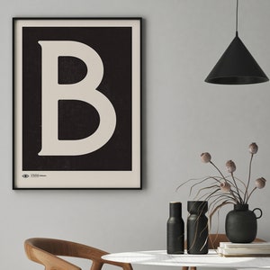 Peut inclure: Une affiche noire et blanche avec une grande lettre blanche "B" sur un fond noir. L'affiche est encadrée en noir et accrochée à un mur blanc.