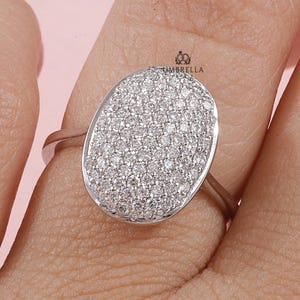 Puede incluir: Un anillo de plata con una gran piedra central de forma ovalada. La piedra está cubierta de pequeños diamantes brillantes.