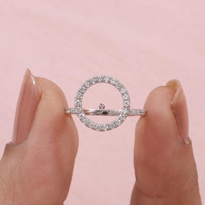 May include: A silver ring with a circular design, encrusted with small, sparkling stones. The ring features a delicate band and a central open circle, creating a modern and elegant look. The word "UMBRELLA" is engraved on the ring.