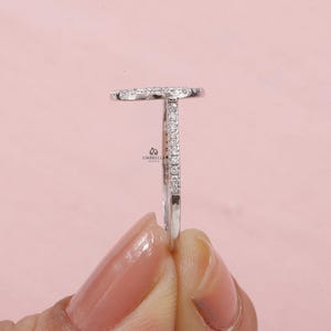 May include: A side view of a silver ring with a diamond-studded oval top and a diamond-lined band. The ring is held against a soft pink background. The brand name "UMBRELLA JEWELS" is visible.