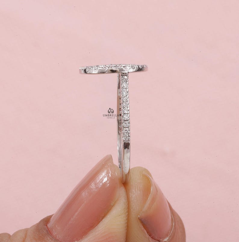 May include: A side view of a silver ring with a diamond-studded oval top and a diamond-lined band. The ring is held against a soft pink background. The brand name "UMBRELLA JEWELS" is visible.