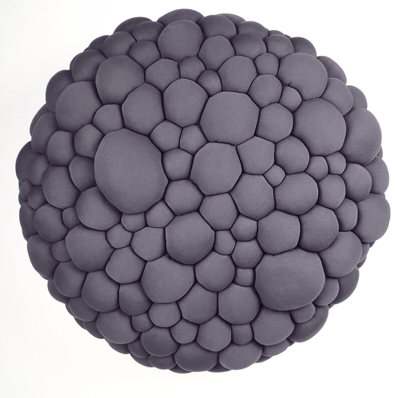 May include: A spherical, gray decorative object with a textured surface composed of numerous, irregularly shaped, rounded protrusions. The object is set against a plain white background, emphasizing its unique, organic form.