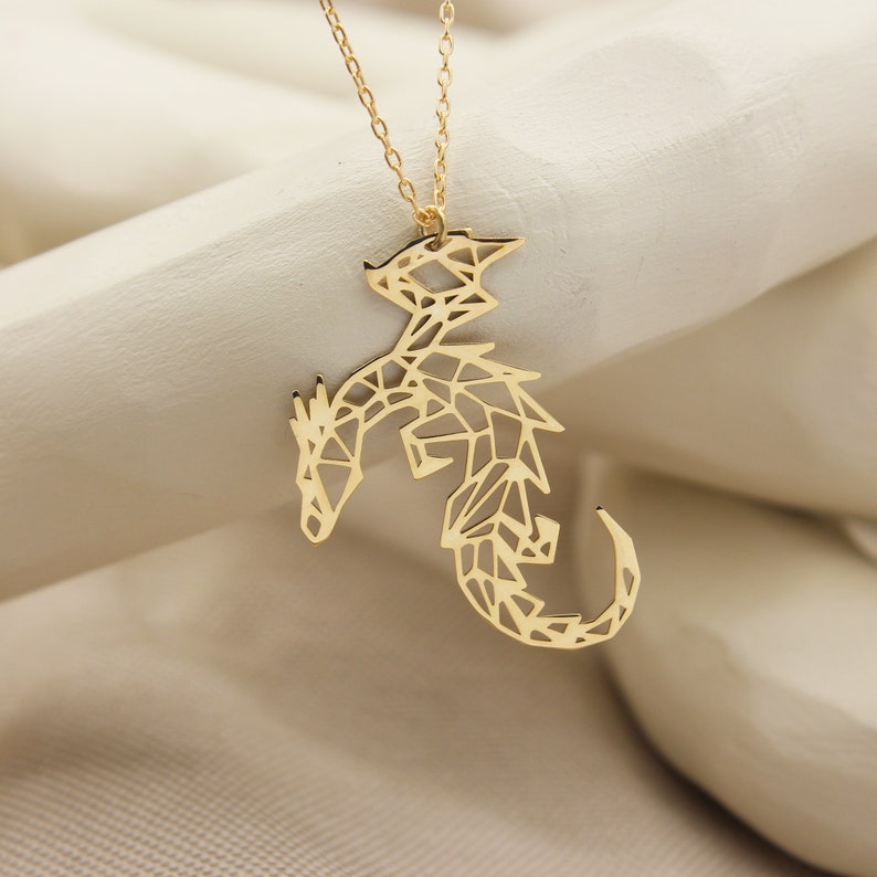 May include: Gold necklace with a geometric dragon pendant. The dragon is made of a delicate, openwork design.