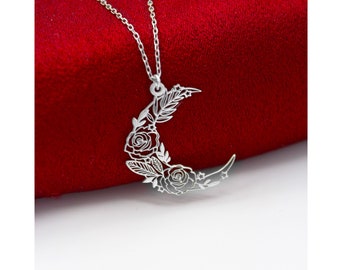 May include: A silver necklace with a crescent moon pendant featuring a delicate floral design. The pendant is made of metal and has a cutout design of roses and leaves.