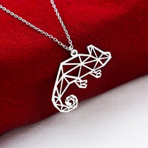 May include: A silver necklace with a geometric chameleon pendant. The pendant is made of triangles and has a detailed design.